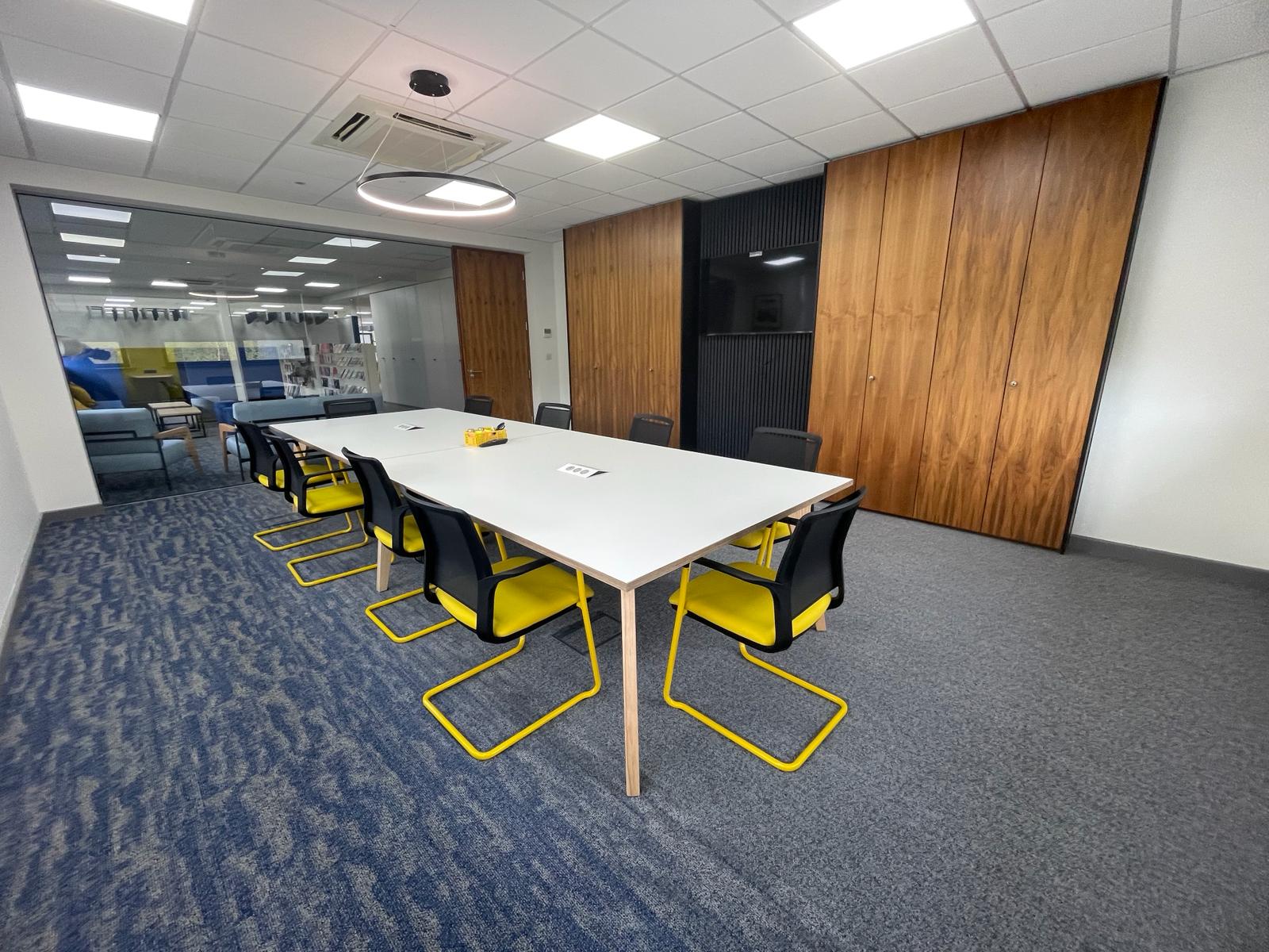 First floor meeting room at Card Factory Wakefield with glazed partitioning, wood effect storage wall and yellow meeting chairs