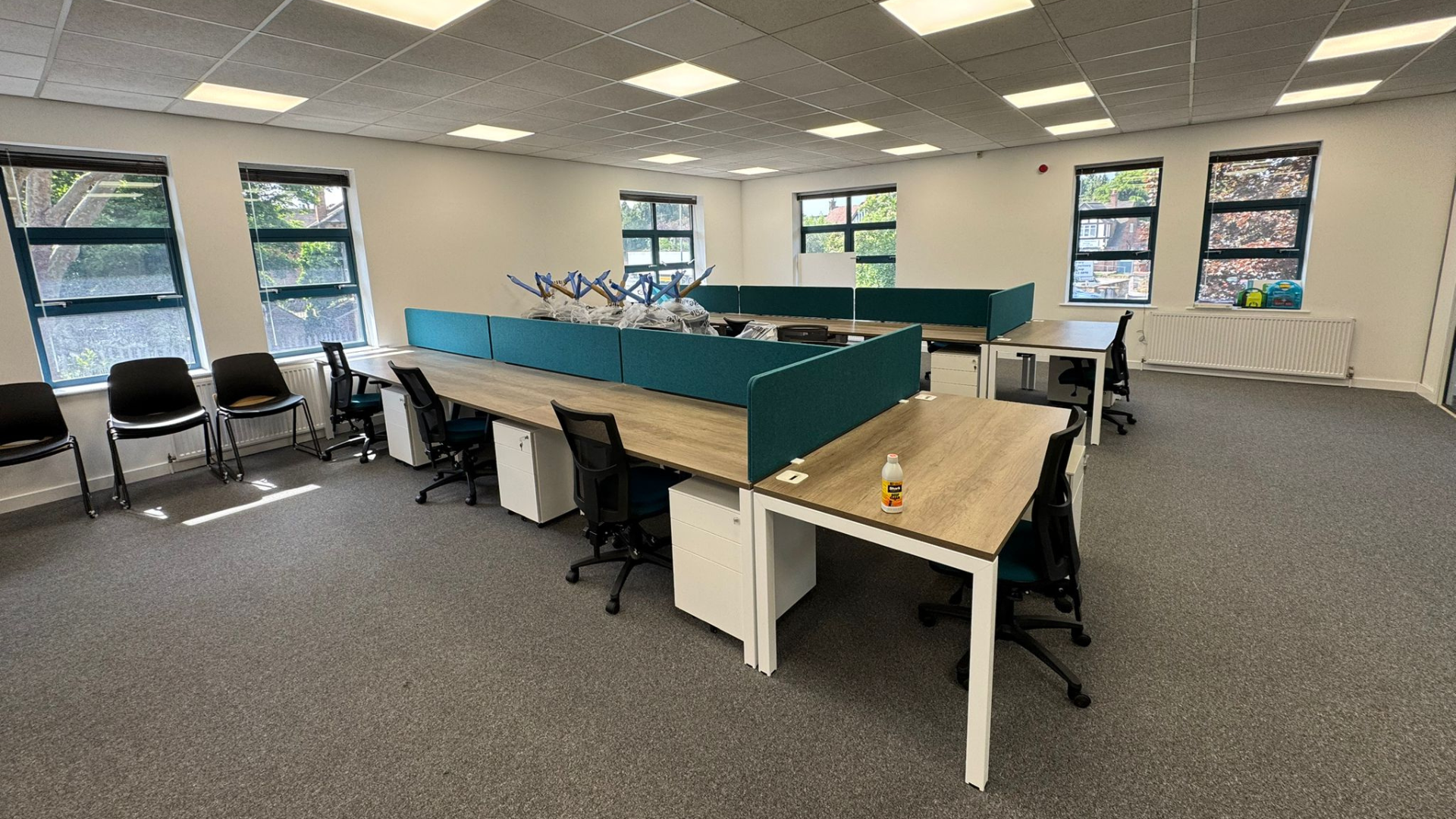 Finished open-plan office for the DSL Systems office fit out featuring bench desks, teal acoustic screens, task chairs and natural light from side windows