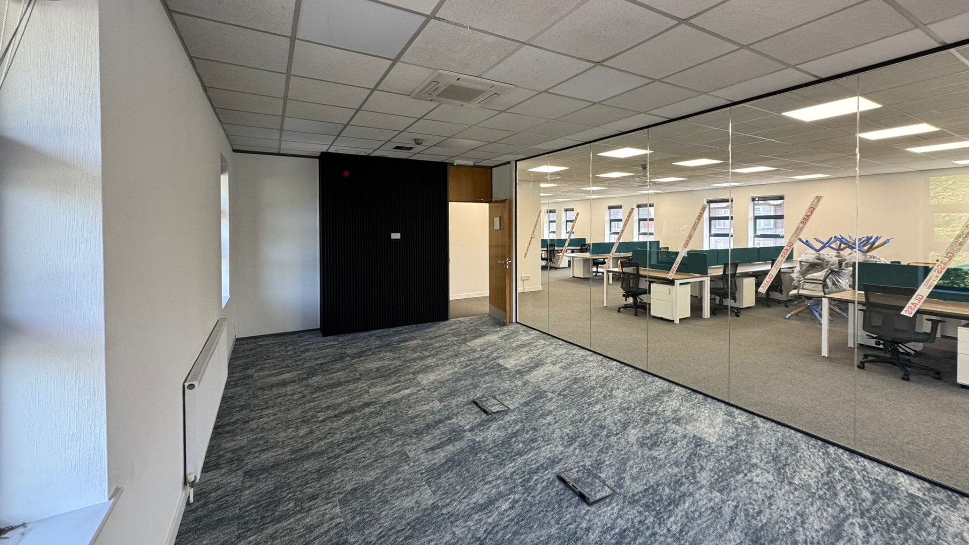 Glazed boardroom installed during the DSL Systems office fit out with feature carpet, black wall panelling and views into the open-plan workspace