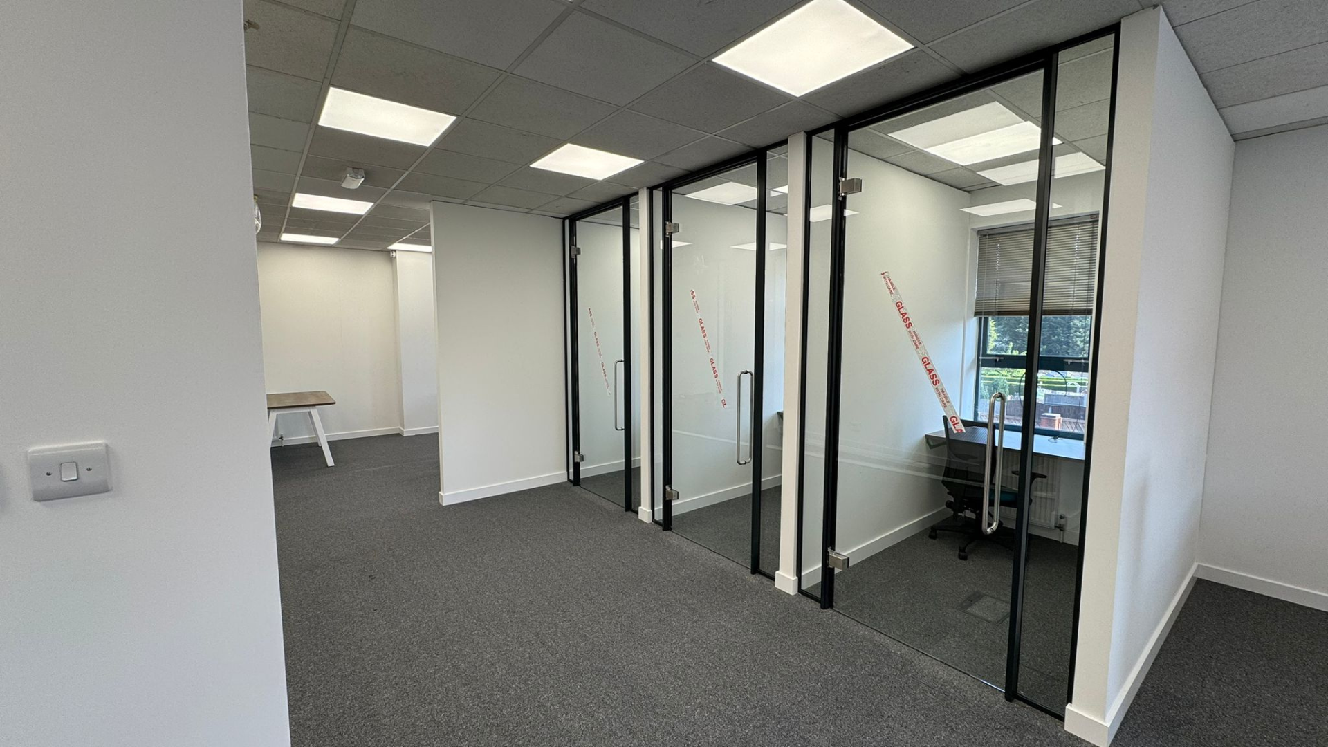 Glass-fronted Teams rooms created for the DSL Systems office fit out with black framed doors, pull handles and individual workstations inside