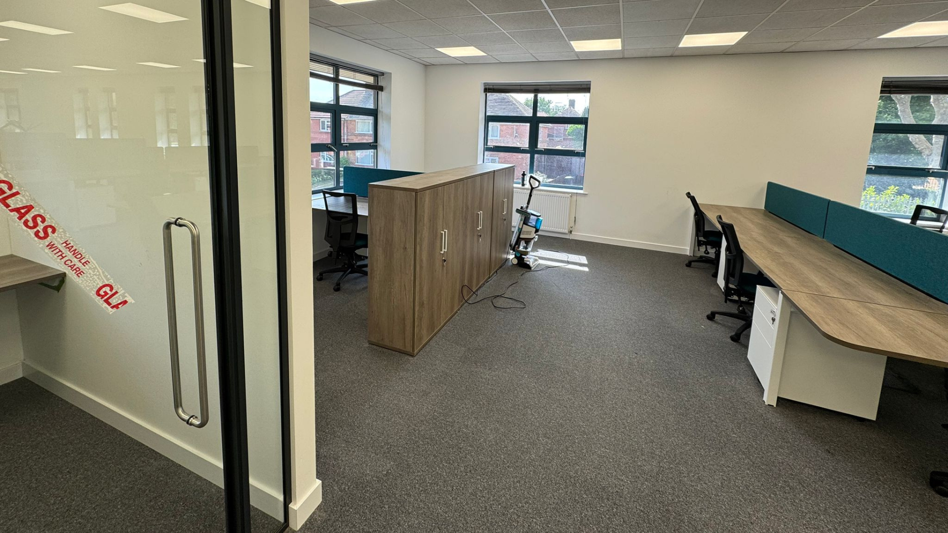 Office furniture and storage installed for the DSL Systems office fit out with desks, chairs, teal screens and wooden storage units near the windows