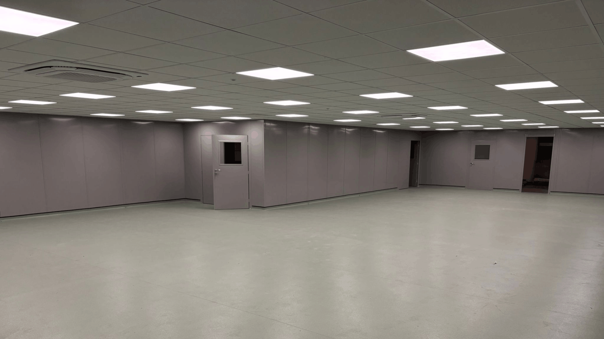 Finished clean room area showing grey steel partition walls, suspended ceiling, LED lighting and open floor space.