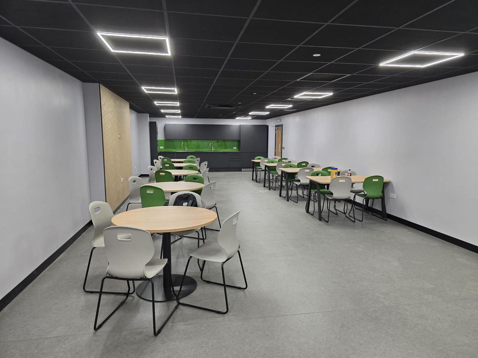 Completed Sertec welfare area refurbishment showing canteen tables, green and grey chairs, black ceiling, safety vinyl flooring and new teapoint